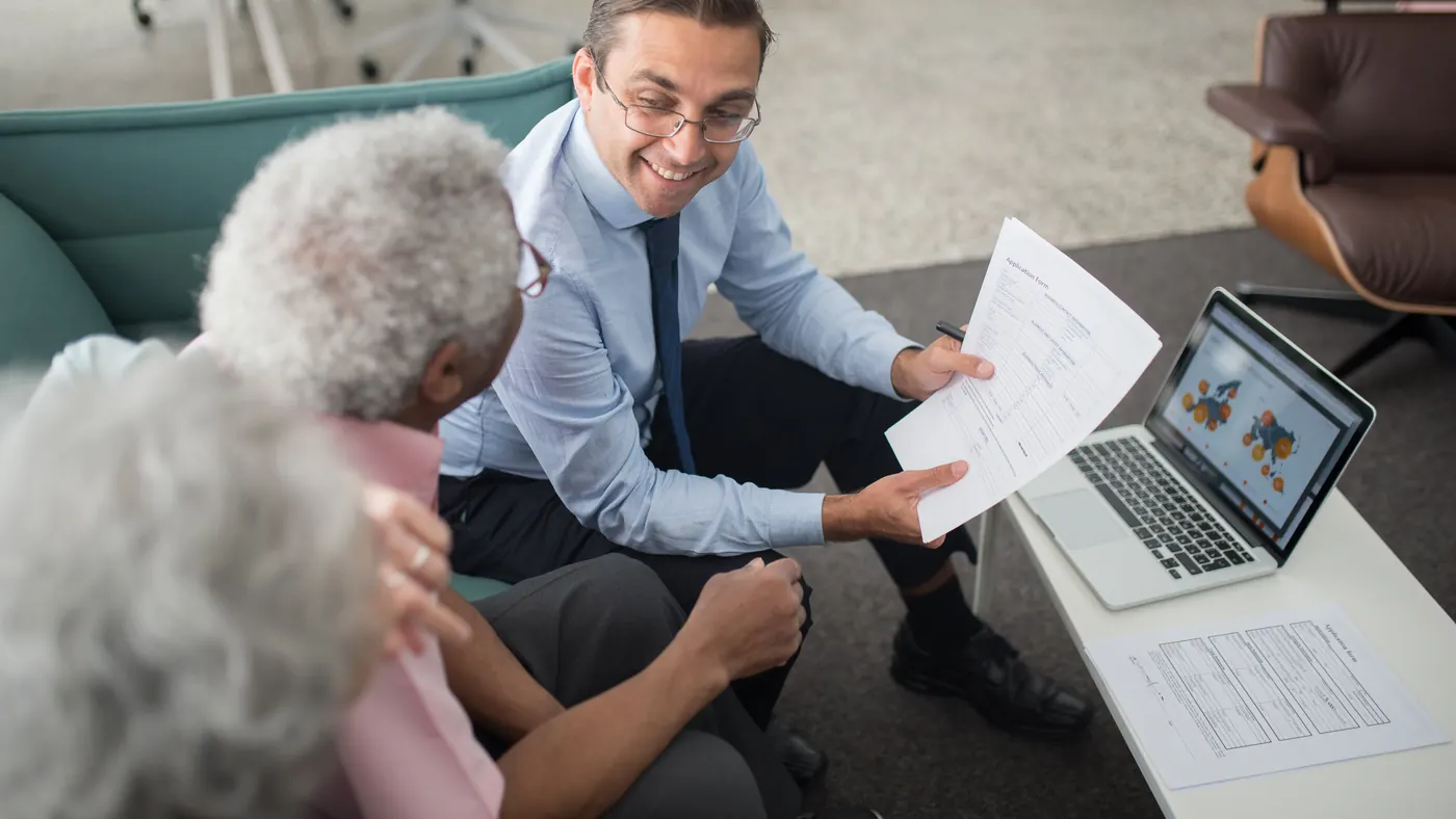 A financial advisor showing a printed plan to an older couple in a living room