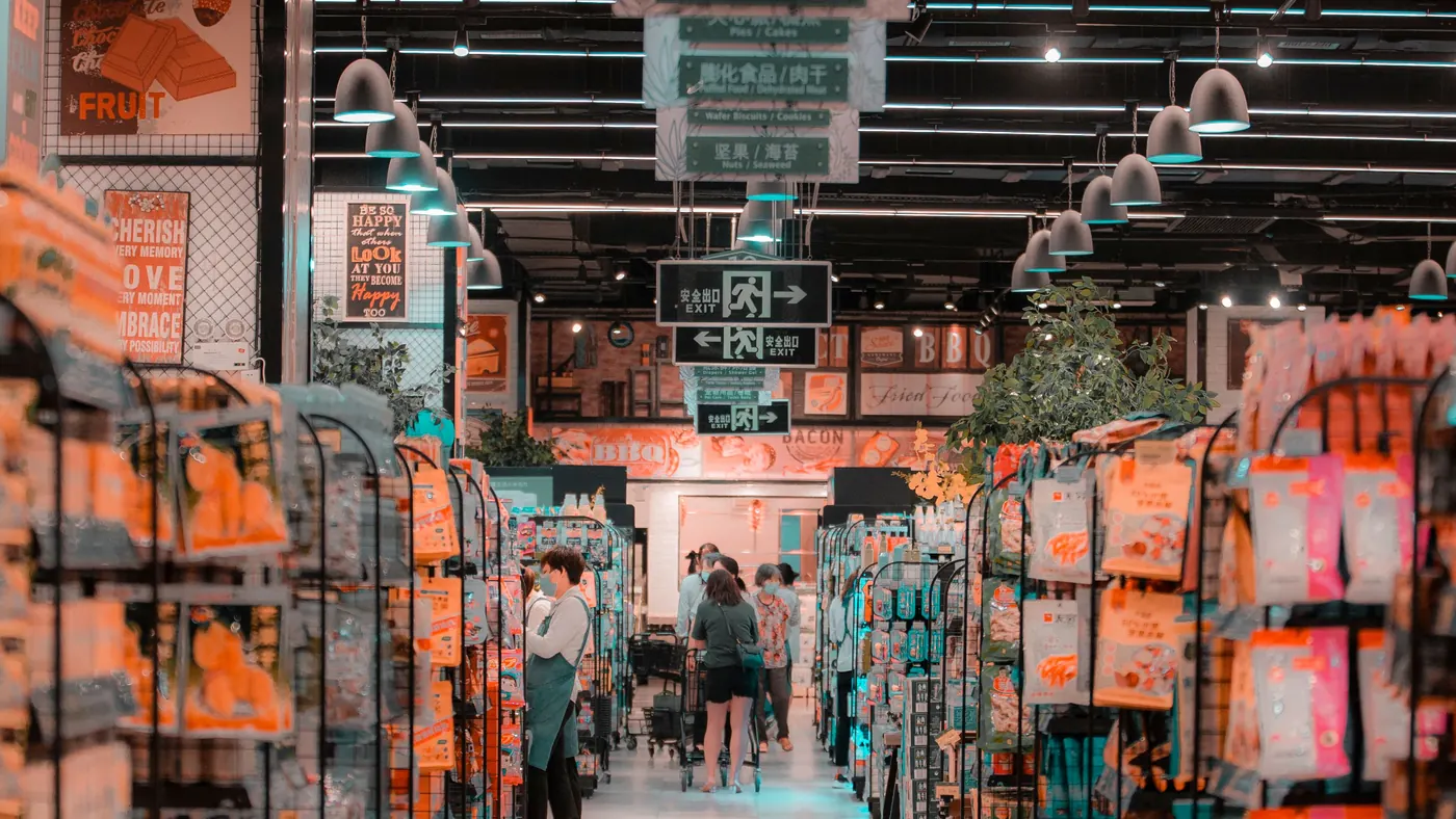 A busy supermarket aisle with shoppers pushing trolleys between full shelves
