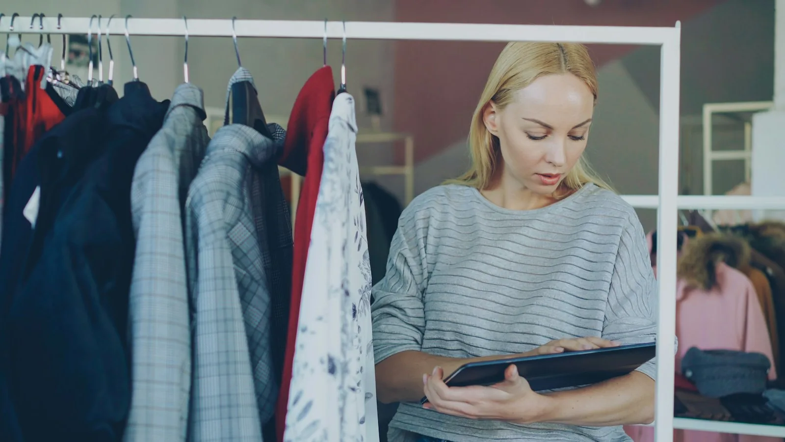 A store manager reviewing stock on a tablet beside a rail of garments