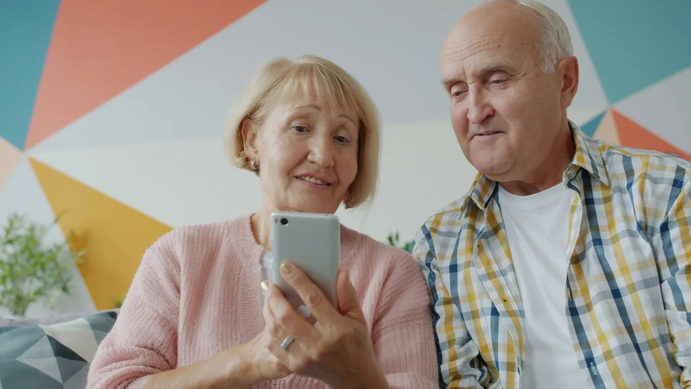 An older couple on a sofa reading an answer on a smartphone together