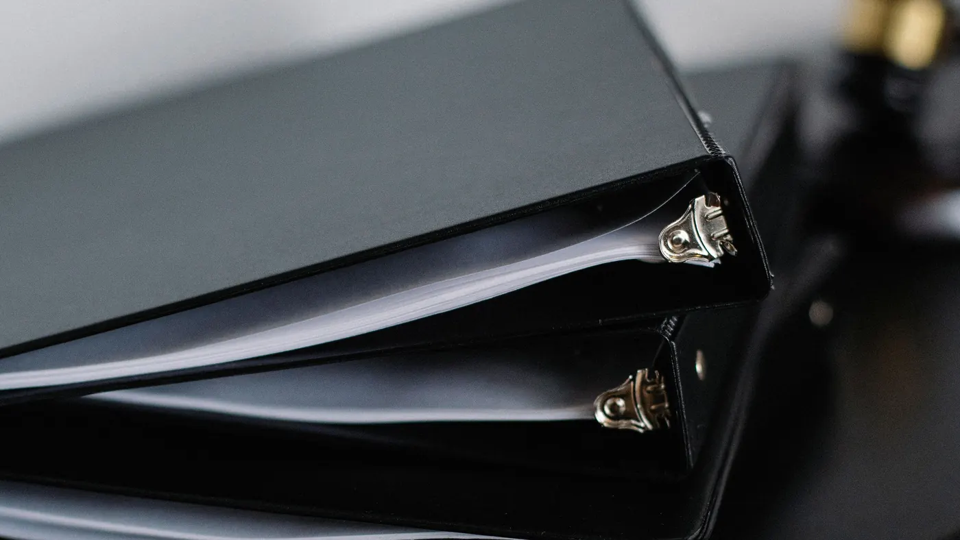A stack of black ring binders full of papers on a dark desk