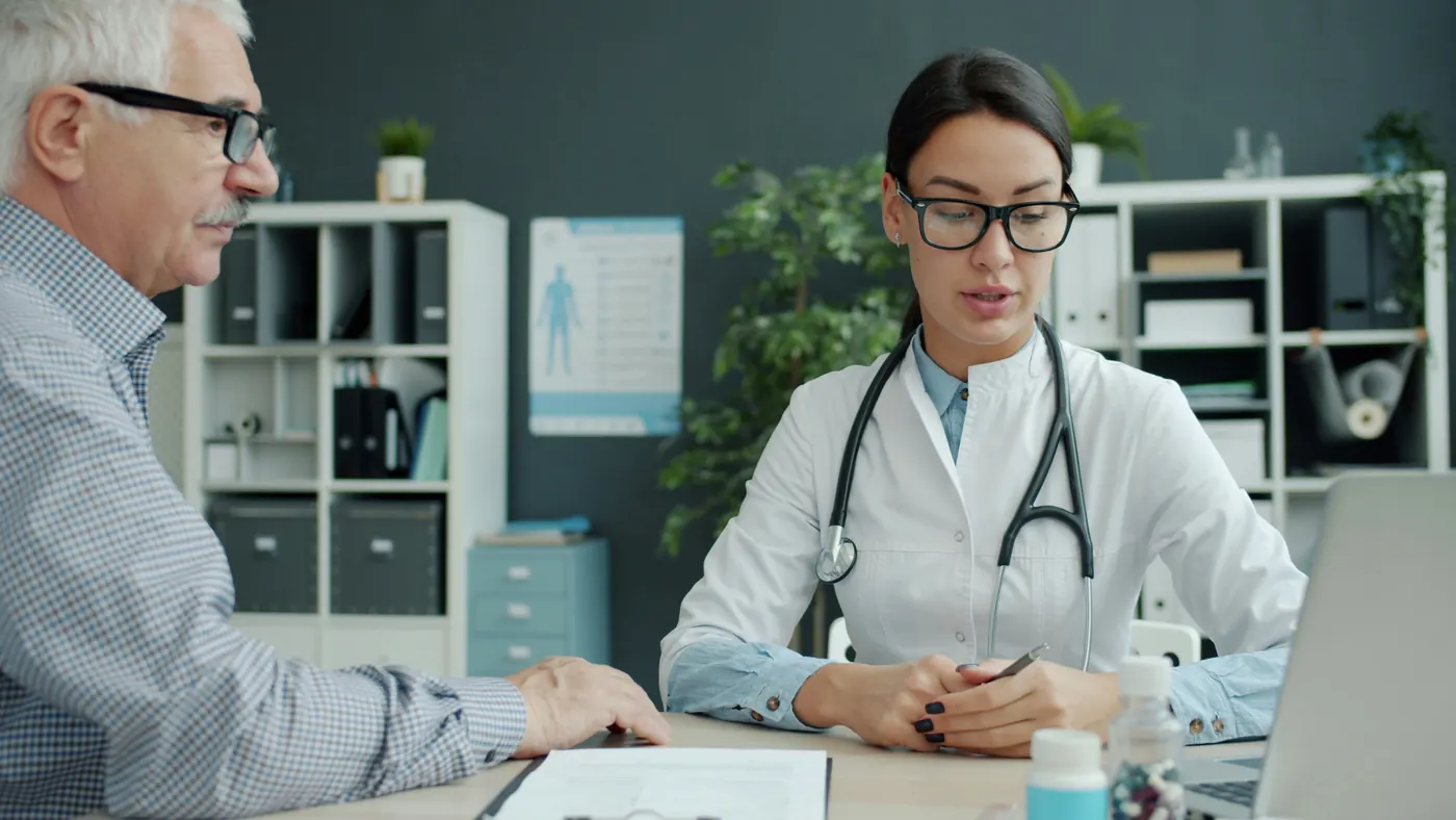 A doctor at her desk talking with an older man about his care