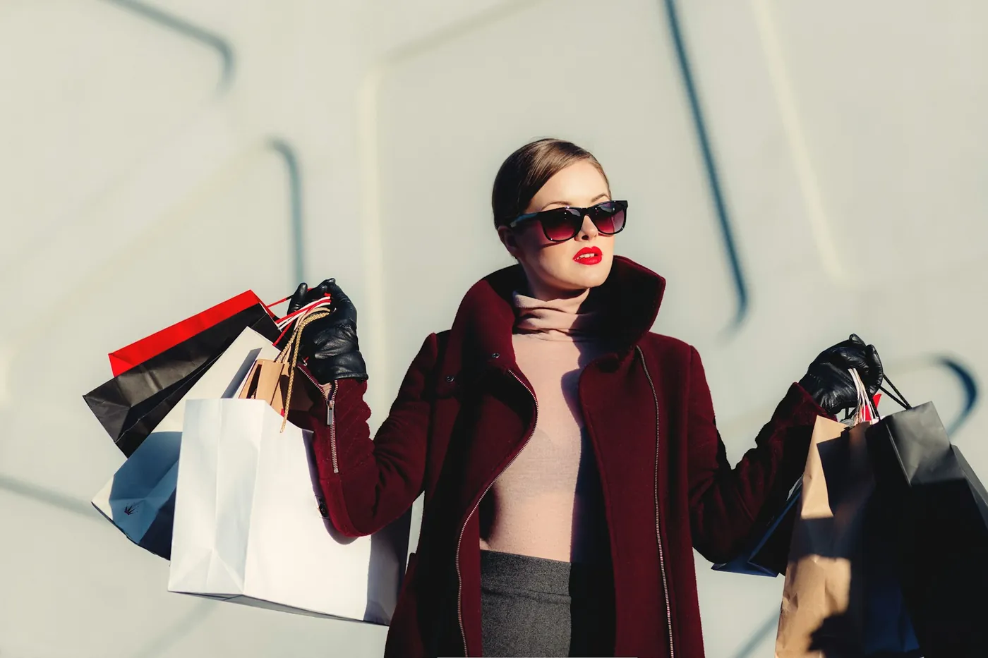 A shopper in sunglasses and a burgundy coat carrying several shopping bags