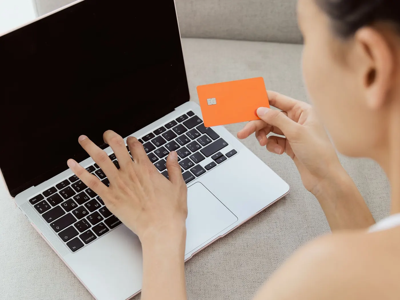 A woman holding a bank card while typing on a laptop at home