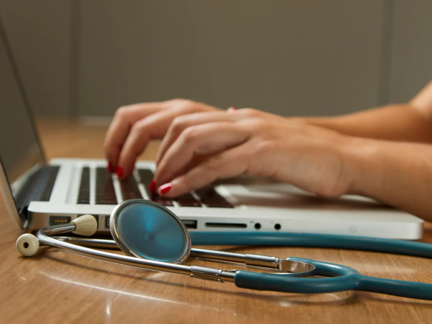 Hands typing on a laptop beside a stethoscope on a clinic desk