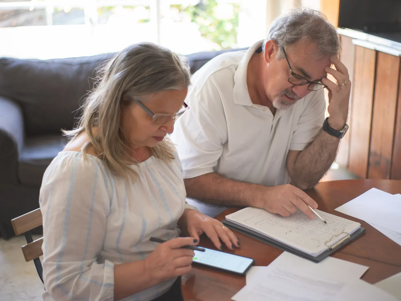 An older couple at a kitchen table going through their finances with papers and a phone