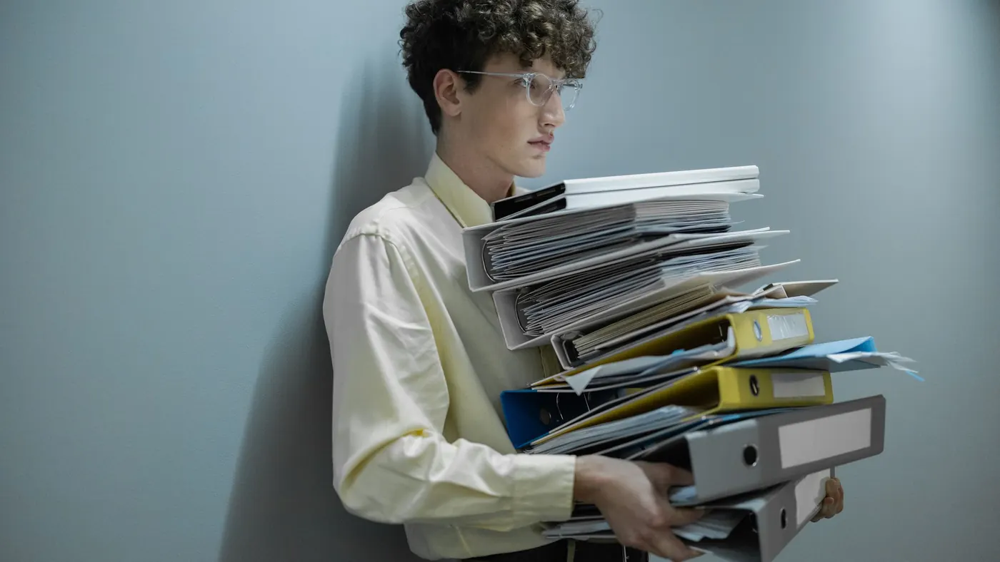 A young office worker carrying a tall stack of folders and binders