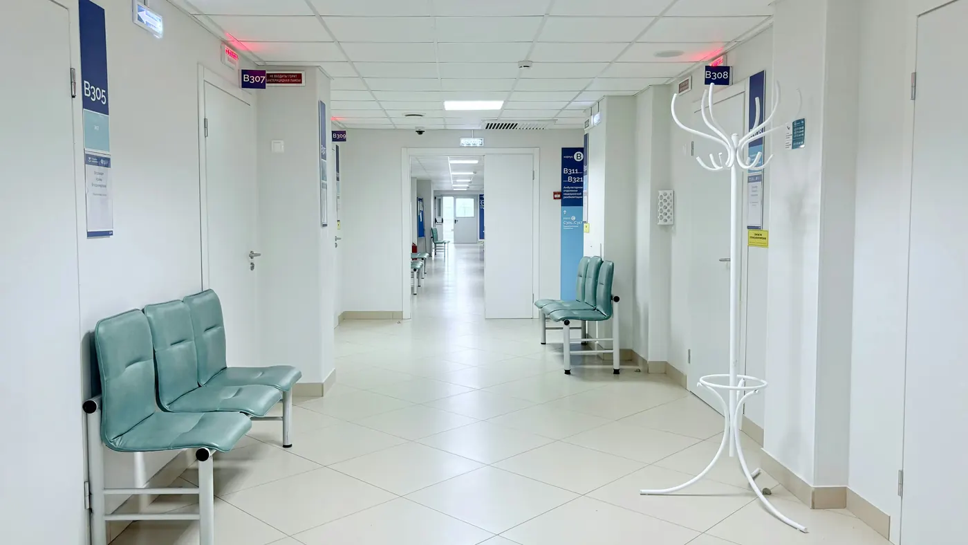 An empty clinic corridor with waiting benches outside consultation rooms
