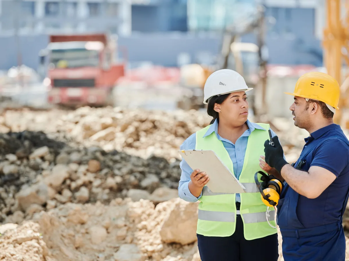 Two hard-hatted colleagues reviewing plans on a tablet on site