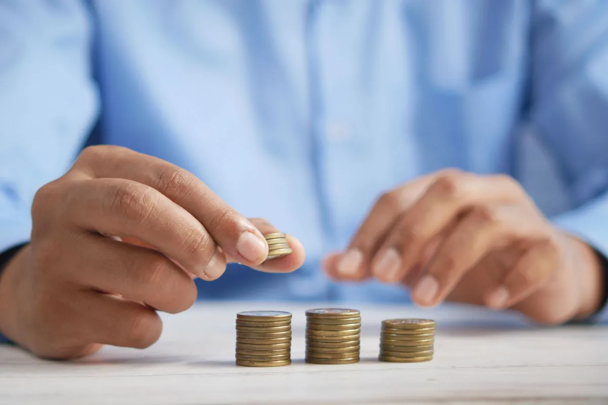 Hands stacking gold coins into rising columns